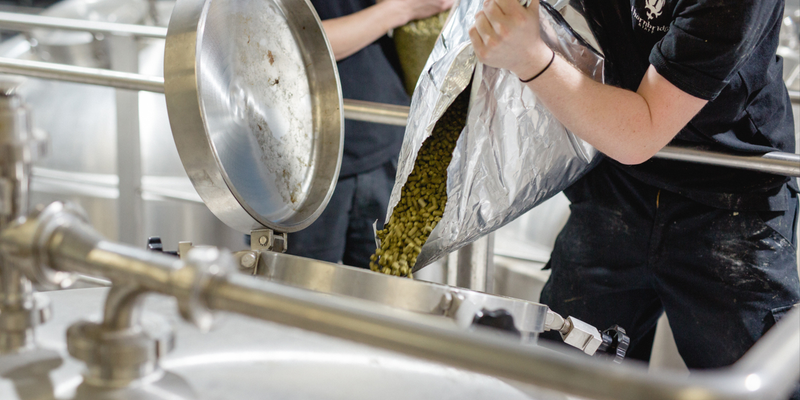 Person pouring green from a bag into a  tank at Thornbridge brewery.