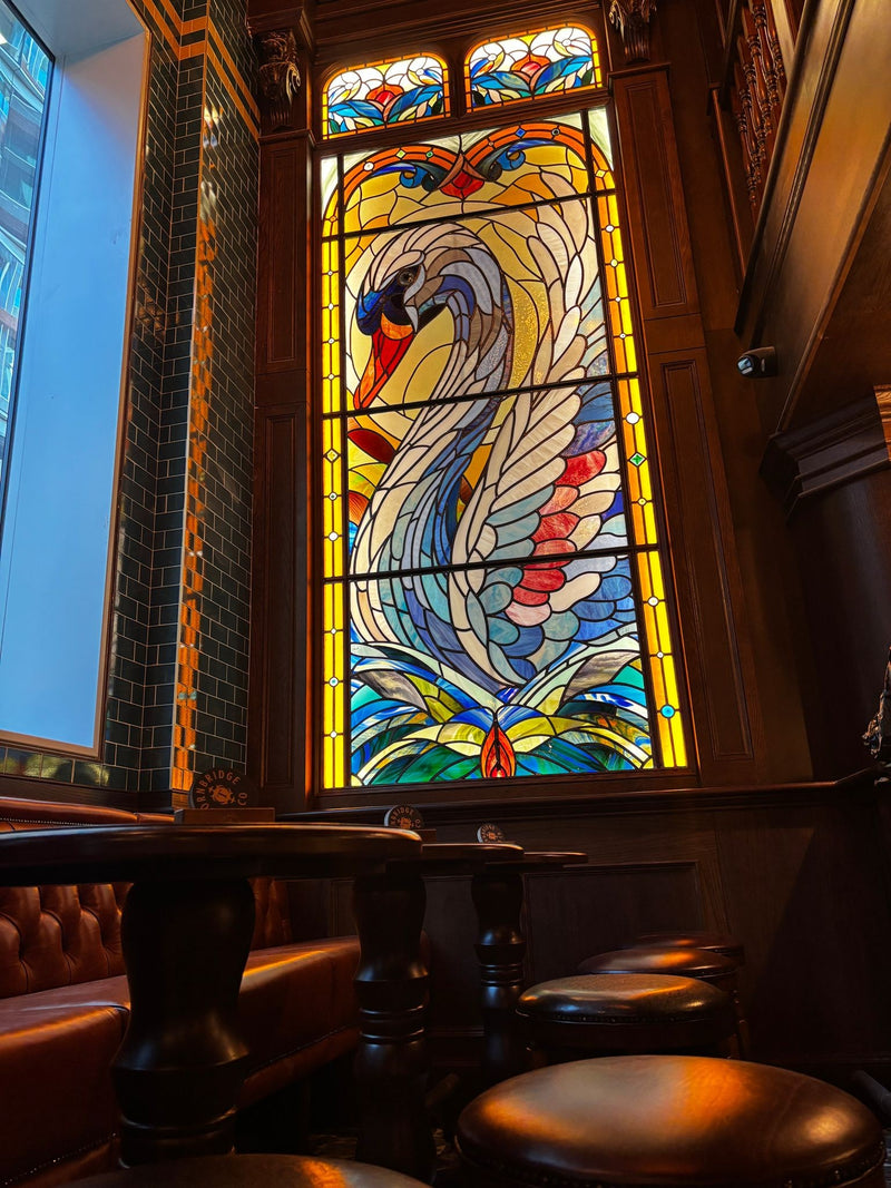Stained glass window with a colorful swan design in The Wild Swan pubs