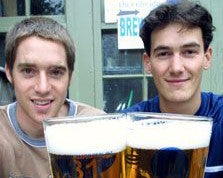 The original brewers holding glasses of beer in front of a window with a sign.
