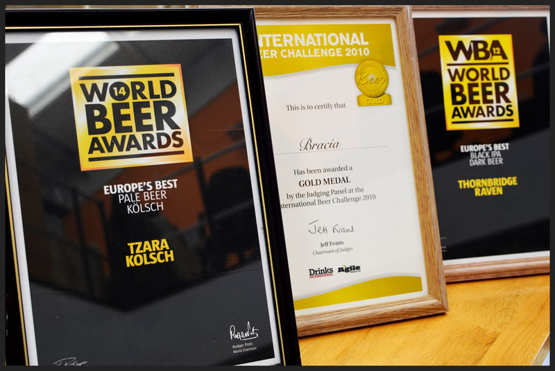 Three framed World Beer Awards certificates displayed on a wooden surface, including the 2010 International Beer Challenge Gold Medal certificate and World Beer Awards editions.